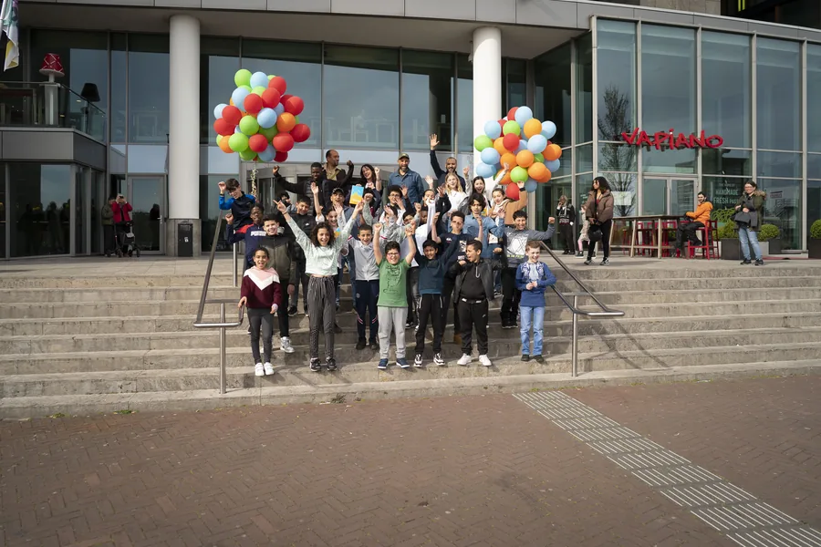 Leerlingen en mentoren van SKC juichen met ballonnen op de trappen voor een theater