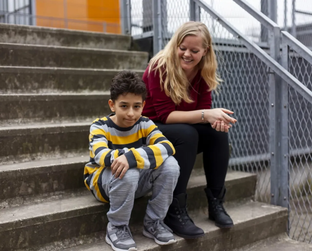Een mentor en een leerling van SKC zitten samen op een trap en lachen